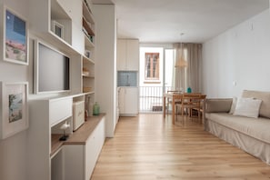 A modern living room with a wooden floor, a sofa, a TV, and a dining area with a table and chairs.