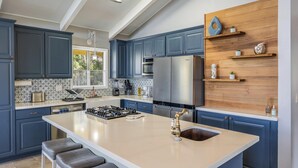 A modern kitchen with blue cabinets, a large island, stainless steel appliances, and wooden shelves. - Beautiful conveniently located 2-bedroom ocean view home in Kailua-Kona.  (Kailua-Kona)