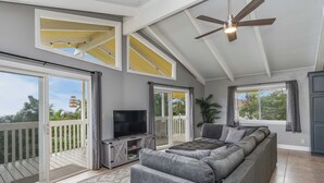 A spacious living room with a large gray sectional sofa, a flat-screen TV, and a ceiling fan. - Beautiful conveniently located 2-bedroom ocean view home in Kailua-Kona.  (Kailua-Kona)