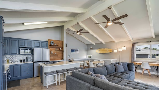 A modern kitchen with grey cabinets, a central island, and a dining area with a grey sofa and chairs. - Beautiful conveniently located 2-bedroom ocean view home in Kailua-Kona.  (Kailua-Kona)