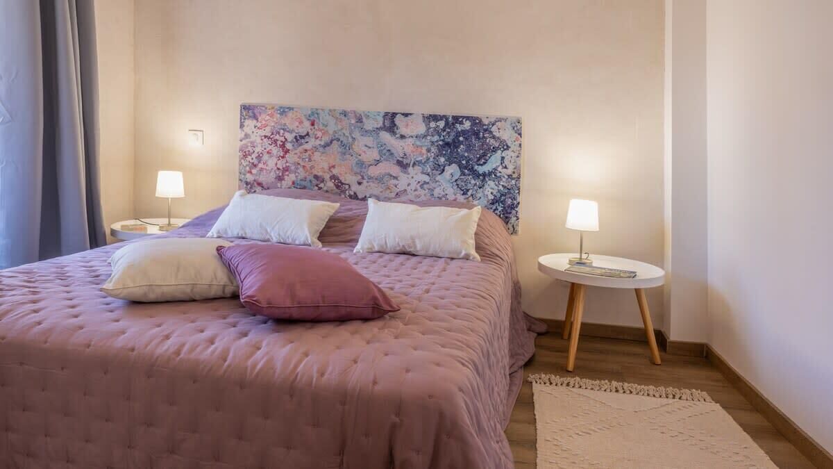 A bedroom with a large bed, two bedside tables with lamps, a floral headboard, and a rug on the floor.