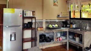 Une cuisine compacte équipée d’un réfrigérateur, d’un four à micro-ondes et d’un évier. Il y a une horloge au mur et une fenêtre avec des rideaux.