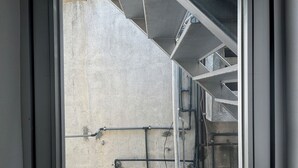 A window with a view of a building's exterior, including a concrete wall and metal structures. - LANAI HOTEL AND Dormitory (Naha)