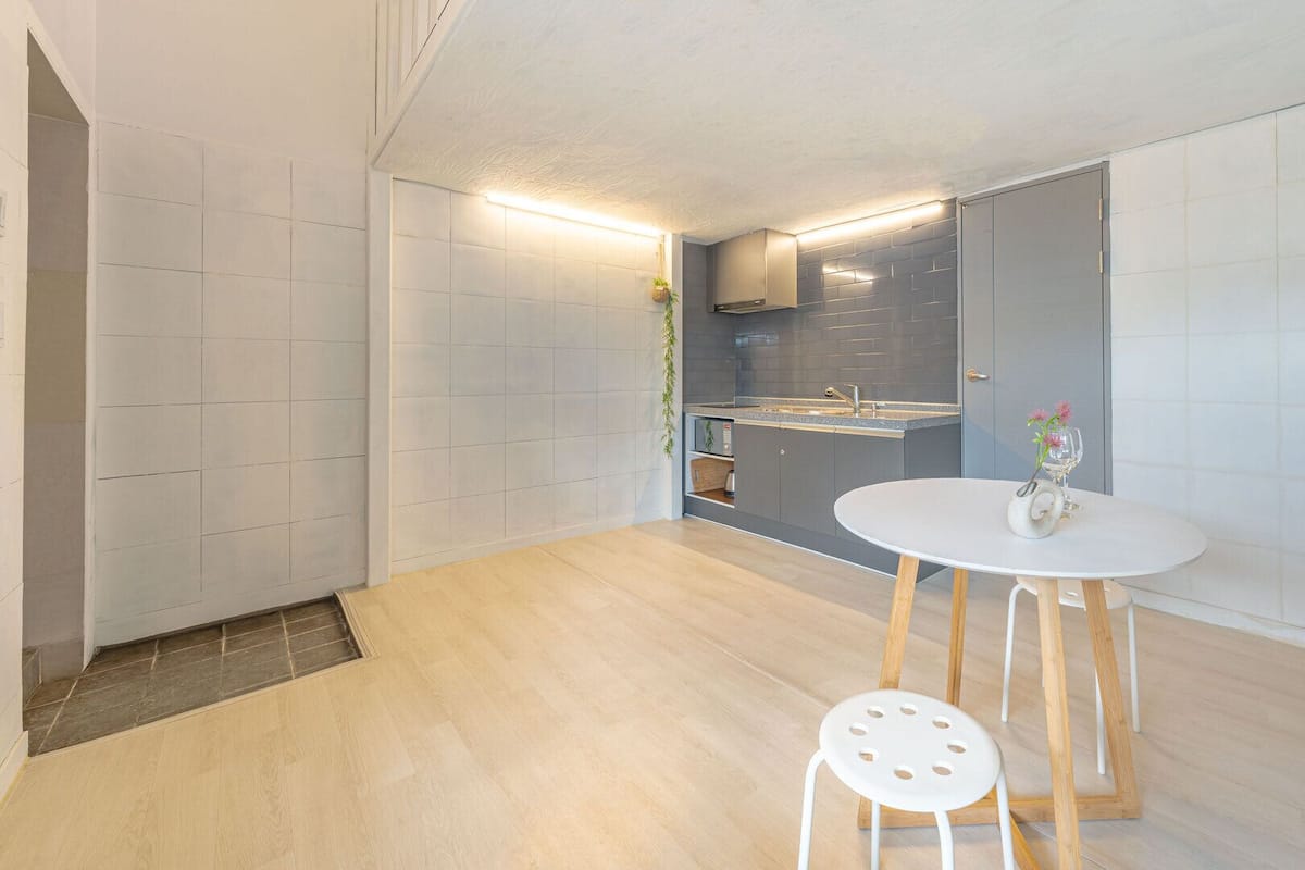 A modern kitchen with grey tiles, a white dining table with two stools, and a small potted plant.