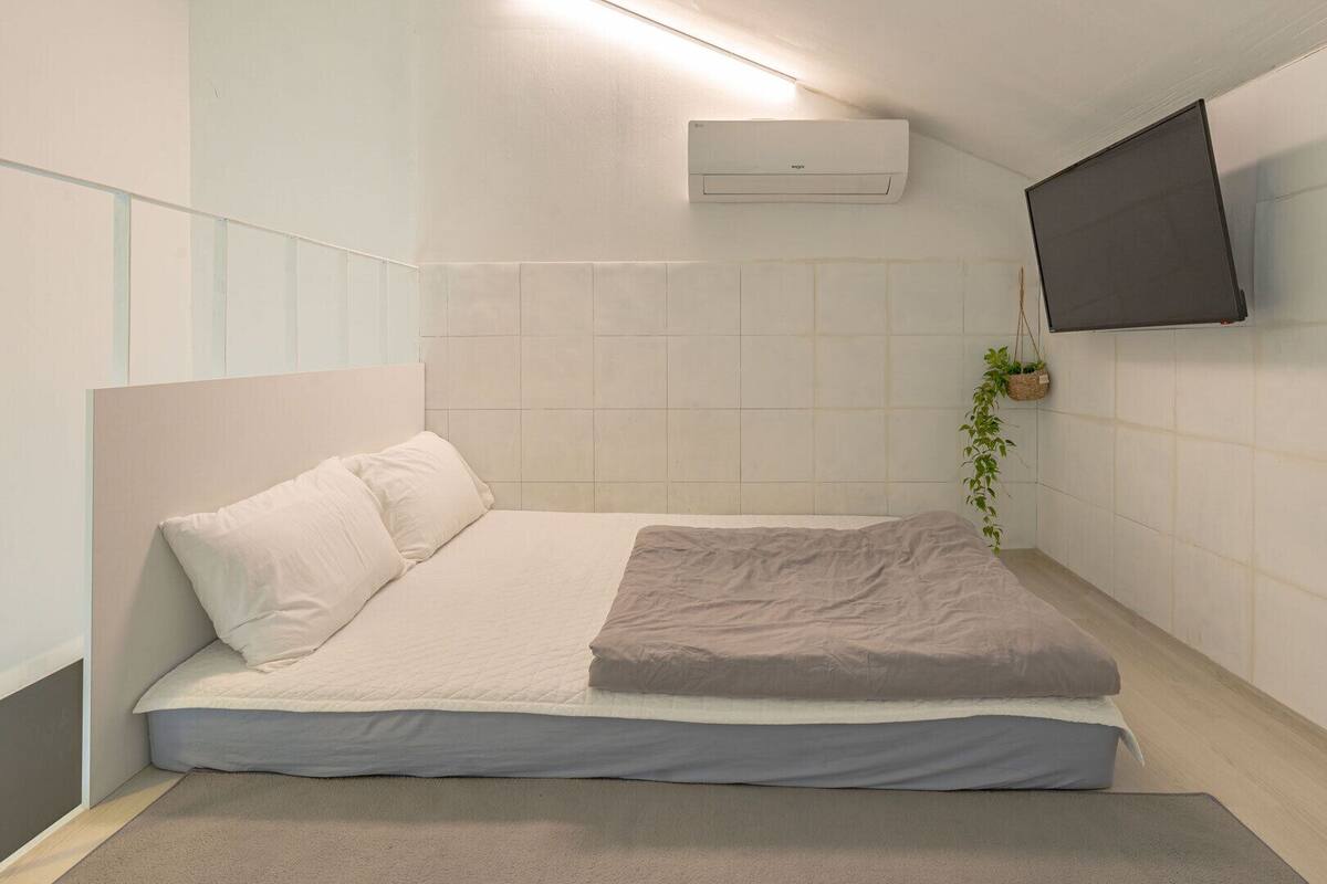A small, modern bedroom with a bed, a wall-mounted air conditioner, and a TV.