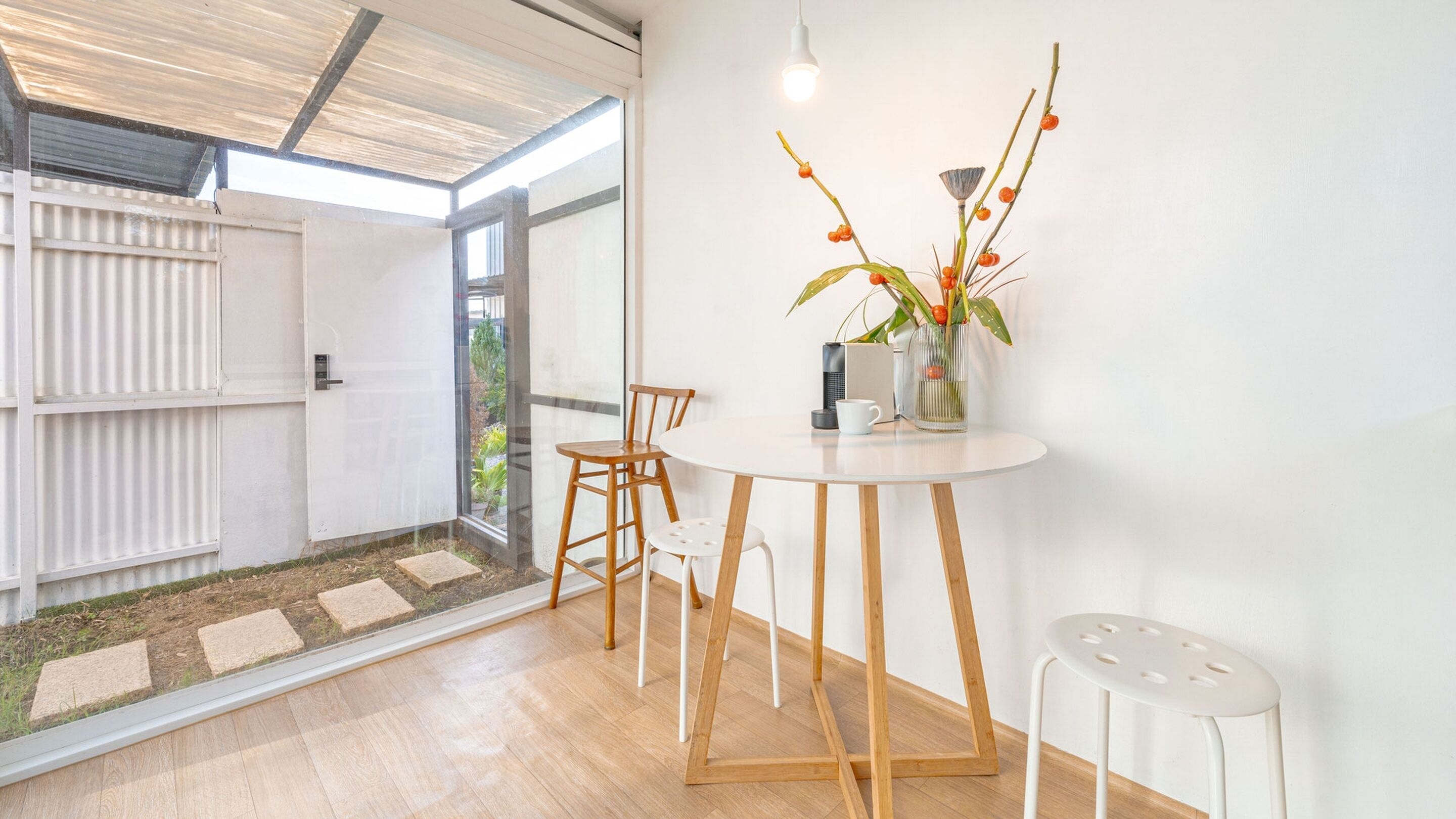 A modern interior with a round table, two chairs, a vase with flowers, and a coffee machine.