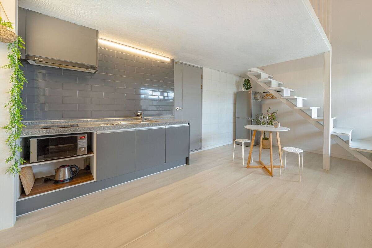 A modern kitchen with grey cabinetry, a built-in oven, and a stainless steel range hood.