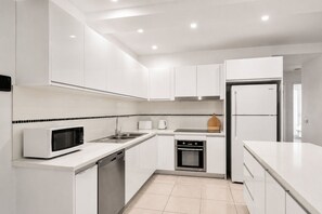 A modern kitchen with white cabinetry, a microwave, a sink, an oven, and a refrigerator.