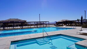 Un espace piscine comprenant plusieurs piscines, des chaises longues et un coin salon abrité.