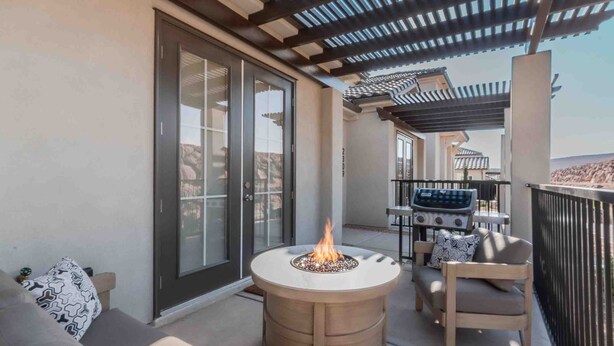 Un balcon doté d’un foyer rond, d’un barbecue et d’un espace salon avec un canapé et un fauteuil.