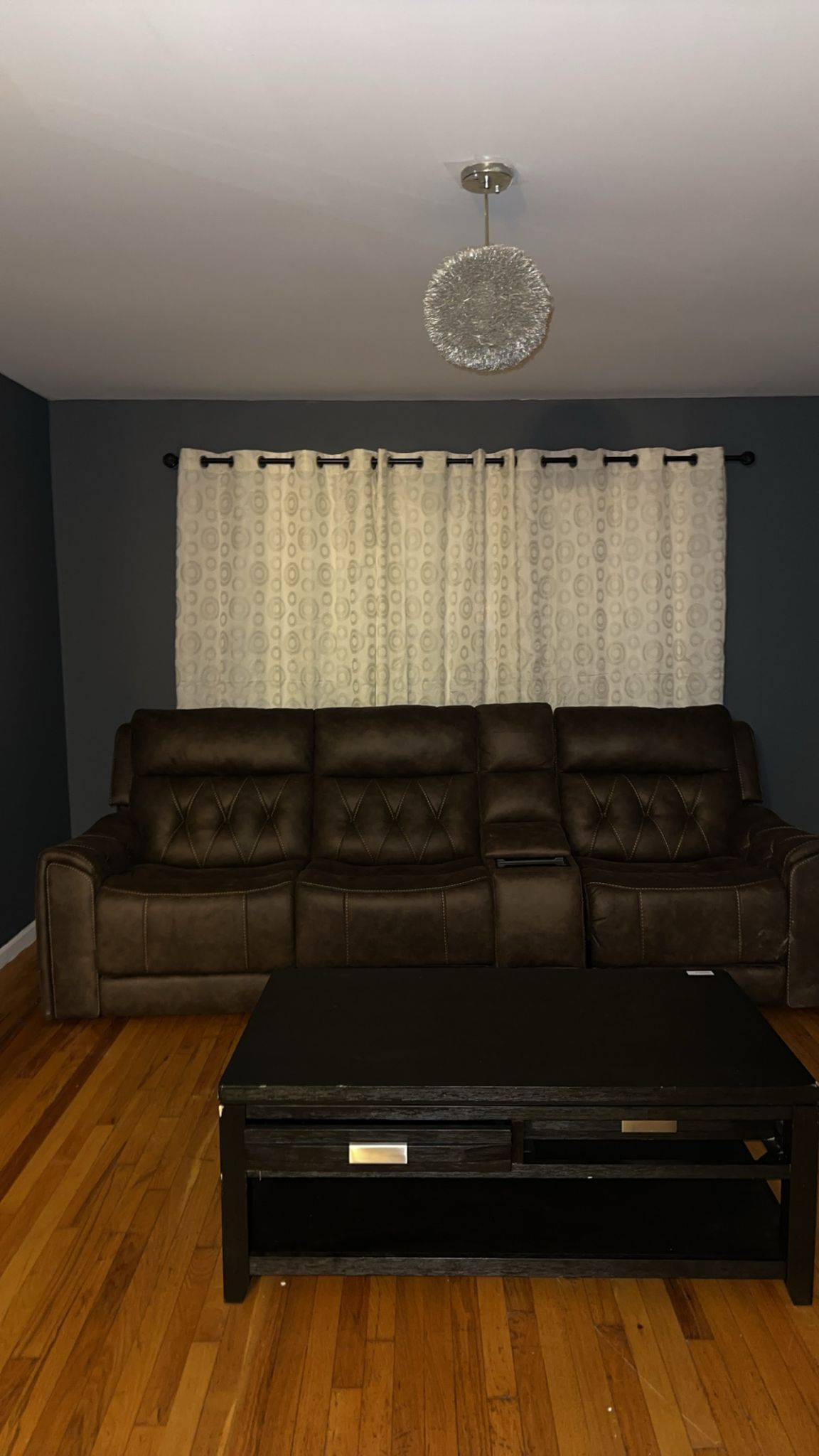 A living room with a dark brown leather sofa, a black coffee table, and a patterned curtain.