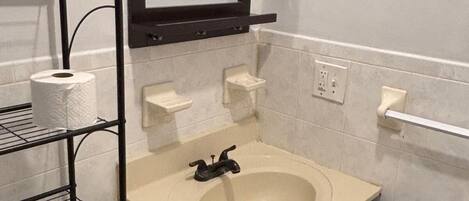 A bathroom with a sink, mirror, and shelves.