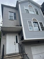A two-story house with a white front door, a garage door, and a brick foundation.