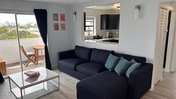 Ein modernes Wohnzimmer mit einem dunkelgrauen Sofa, einem Glastisch und Blick auf die Stadt vom Balkon aus.