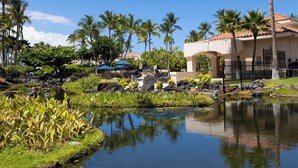 Un complexe hôtelier tropical doté d’un étang, de palmiers et d’un bâtiment surmonté d’un toit en tuiles.