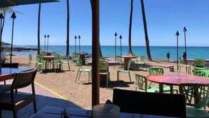 Un restaurant situé en bord de mer, avec une terrasse, des tables et des chaises, offrant une vue sur l’océan.