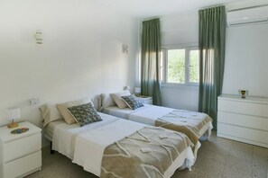 A double room with two beds, a bedside table with a lamp, a dresser, and a window with curtains.