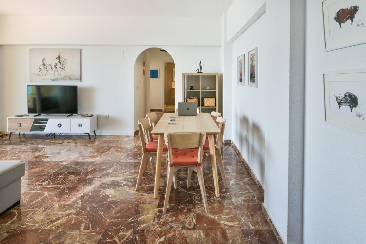 Una sala de estar moderna con piso de mármol, una mesa de comedor con sillas, un televisor en un mueble y obras de arte en las paredes.