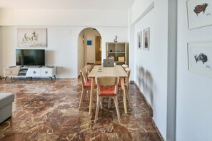 Un saló modern amb terra de marbre, una taula de dinar amb caires, un televisor sobre un moble i obres d'art a les parets.