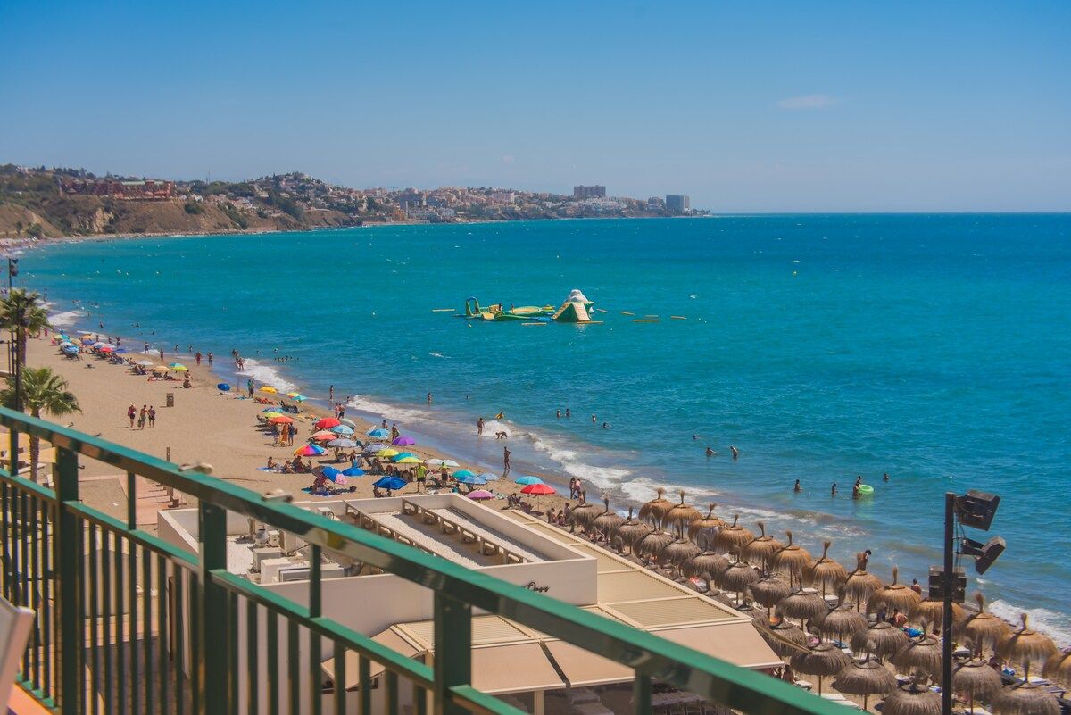 A beach with umbrellas, people, and a clear sky.