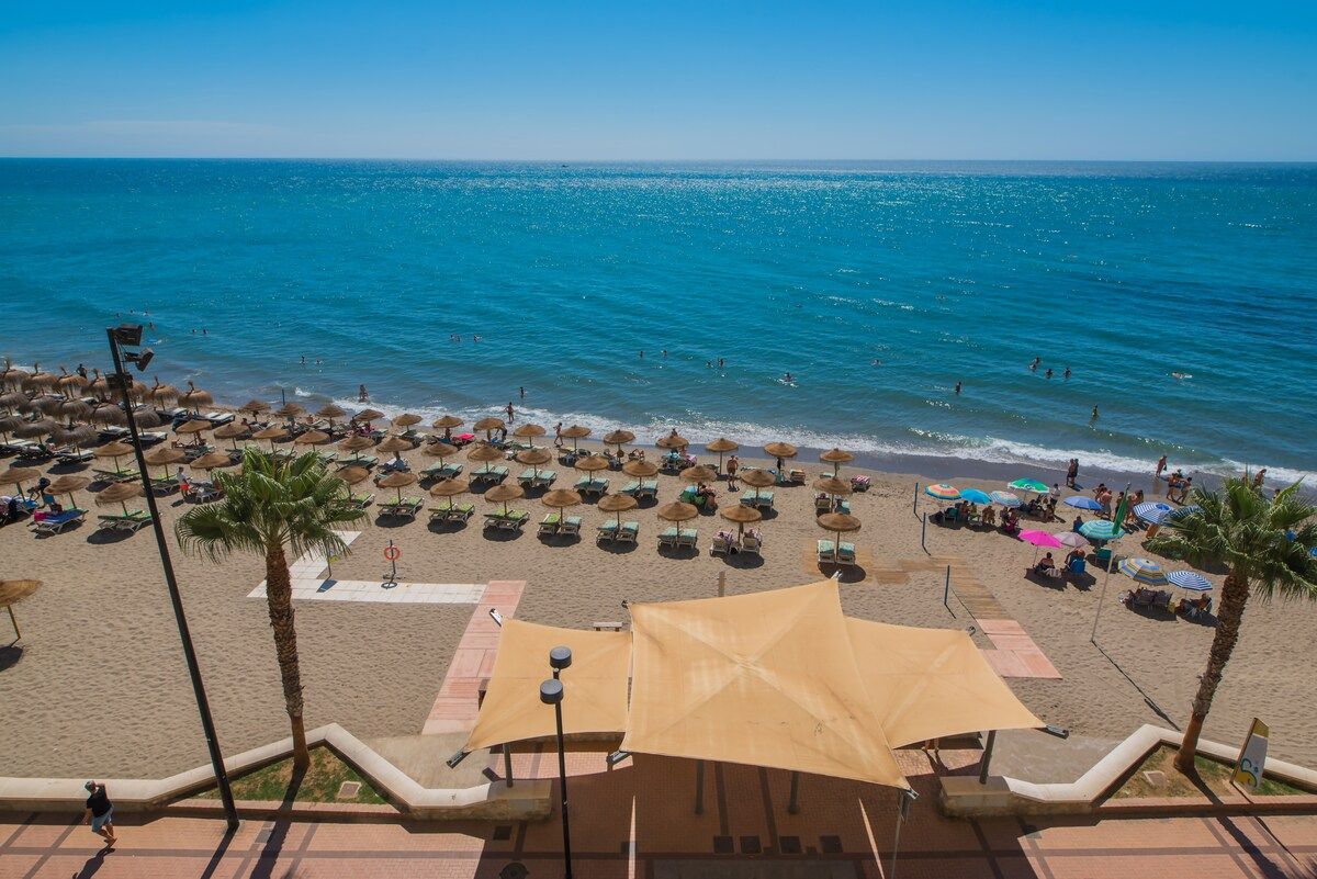 A beach with umbrellas and lounge chairs, a clear sky, and the ocean.