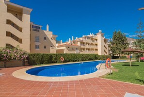 A swimming pool with a tiled deck, surrounded by a building with balconies and a clear blue sky. - Large pool, balcony & great views. Parking. (Benalmadena)