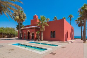 A red building with arched windows and a tower, surrounded by palm trees and a clear blue sky. - Large pool, balcony & great views. Parking. (Benalmadena)