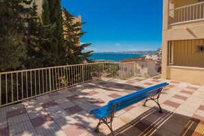 Un balcon avec un banc bleu, une balustrade et une vue sur la mer et les bâtiments.
