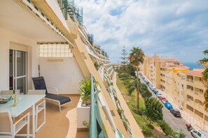 Een balkon met een eettafel en stoelen, uitzicht op een straat met geparkeerde auto's en een rij gebouwen op de achtergrond.