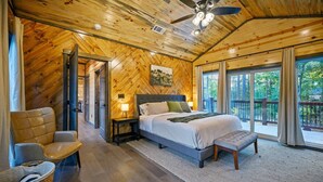 A wooden-paneled bedroom with a bed, a chair, a nightstand, and a large window.