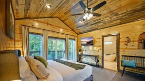 A spacious bedroom with a large bed, a ceiling fan, a TV, a sink, and a bench.