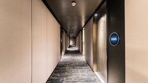 Pasillo de hotel con alfombra estampada, techo con diseño de cuadrícula y una pantalla digital mostrando el número de habitación 5505.