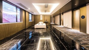 Un vestíbulo de hotel con piso de mármol negro, un sofá blanco y un amplio ventanal.