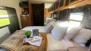 Ein gemütliches Schlafzimmer in einem Wohnmobil, mit einem Bett, Kissen, einer Decke, einer kleinen Pflanze und einem Schild auf dem Nachttisch.
