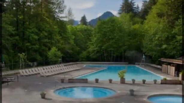 Ein Poolbereich mit mehreren runden Pools und einer zentralen Fontäne, umgeben von Bäumen und einer Berglandschaft.