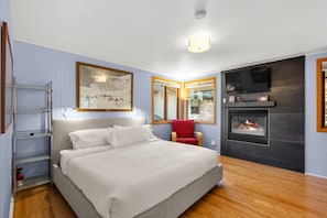 A bedroom with a bed, a red chair, a TV mounted on the wall, and a fireplace. - Snowmass Townhome Near Base Village! Pool/HT, W/D, Gas FP & Parking (Snowmass Village)