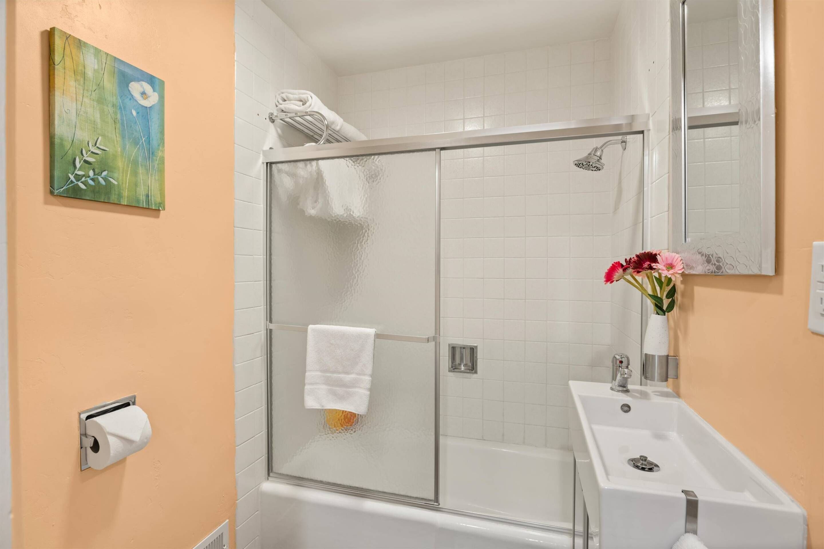 A bathroom with a glass shower enclosure, a white sink, and a mirror.