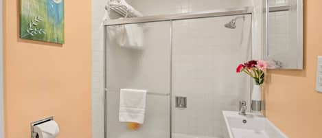 A bathroom with a glass shower enclosure, a white sink, and a mirror.
