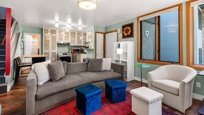 Ein modernes Wohnzimmer mit grauem Sofa, blauen Hocker, einem weißen Sessel und einem roten Teppich mit Muster.