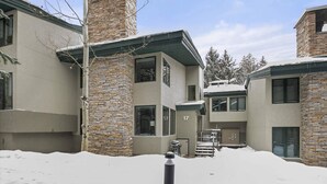 Ein modernes Gebäude mit einem Steinkamin, zahlreichen Fenstern und einem mit Schnee bedeckten Untergrund.