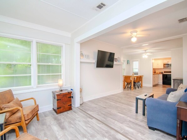 A spacious living area with a dining table, sofa, and a TV mounted on the wall.