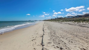 A wide sandy beach with ocean waves, a clear sky, and beachfront properties. - Sojourn's Sea Views with Balcony Sleeps 4 (Virginia Beach)