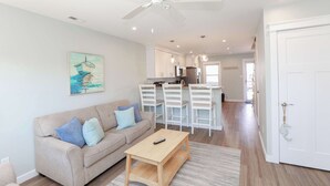A modern living room with a sofa, a coffee table, and a ceiling fan. - Sojourn's Sea Views with Balcony Sleeps 4 (Virginia Beach)