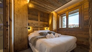 Un dormitorio de cabaña de madera con una cama, una ventana y una lámpara fijada a la pared.