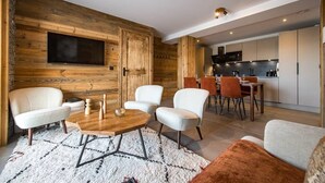 Una sala de estar moderna con una pared de acento de madera, un televisor de pantalla plana y una zona de comedor con una cocina al fondo.