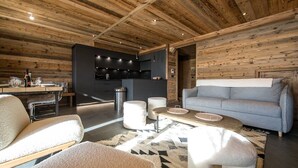 Ein modernes Interieur mit Holzbalkendecke, einem grauen Sofa, einem Esstisch mit Stühlen und einer Küchenzeile.