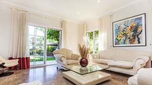 A spacious living room with a glass coffee table, two sofas, and a large window with curtains.