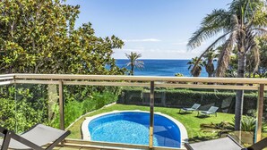 A pool area with a clear view of the ocean, surrounded by lush greenery and palm trees.