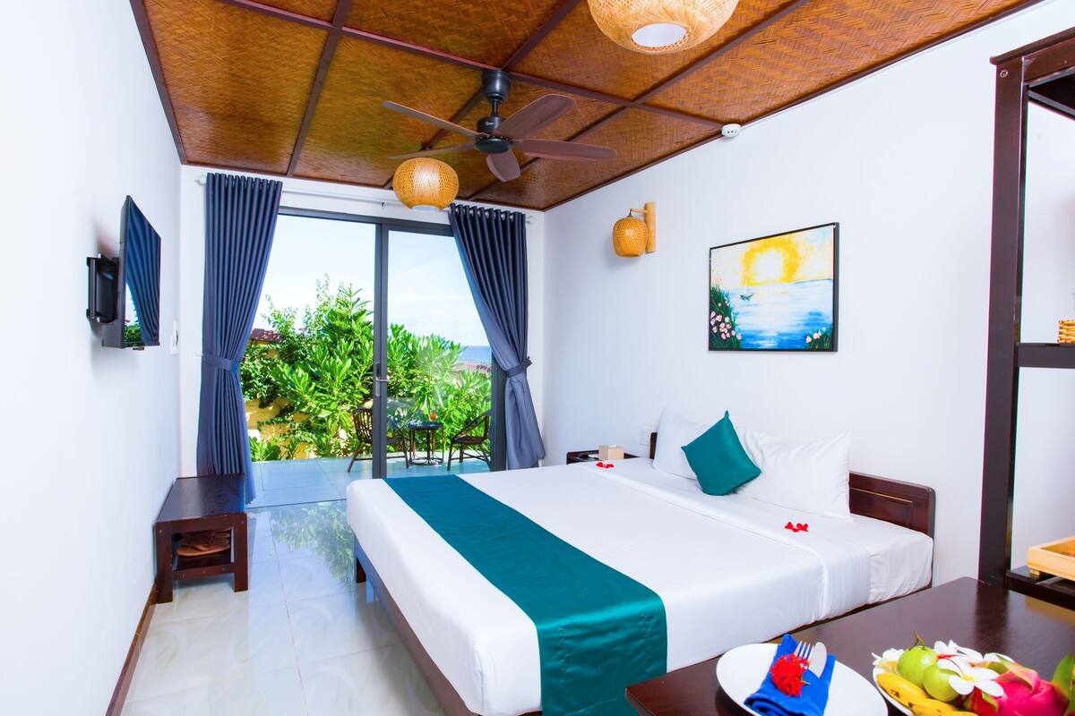 Una habitación de hotel con cama, ventilador de techo, un cuadro y una mesa de comedor con fruta.