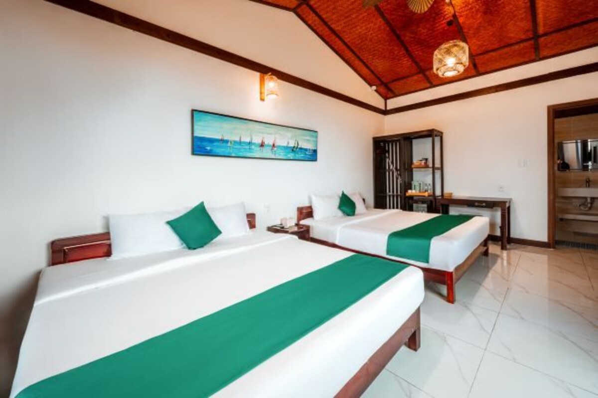 A hotel room with two beds, a desk, a painting, and a ceiling light fixture.